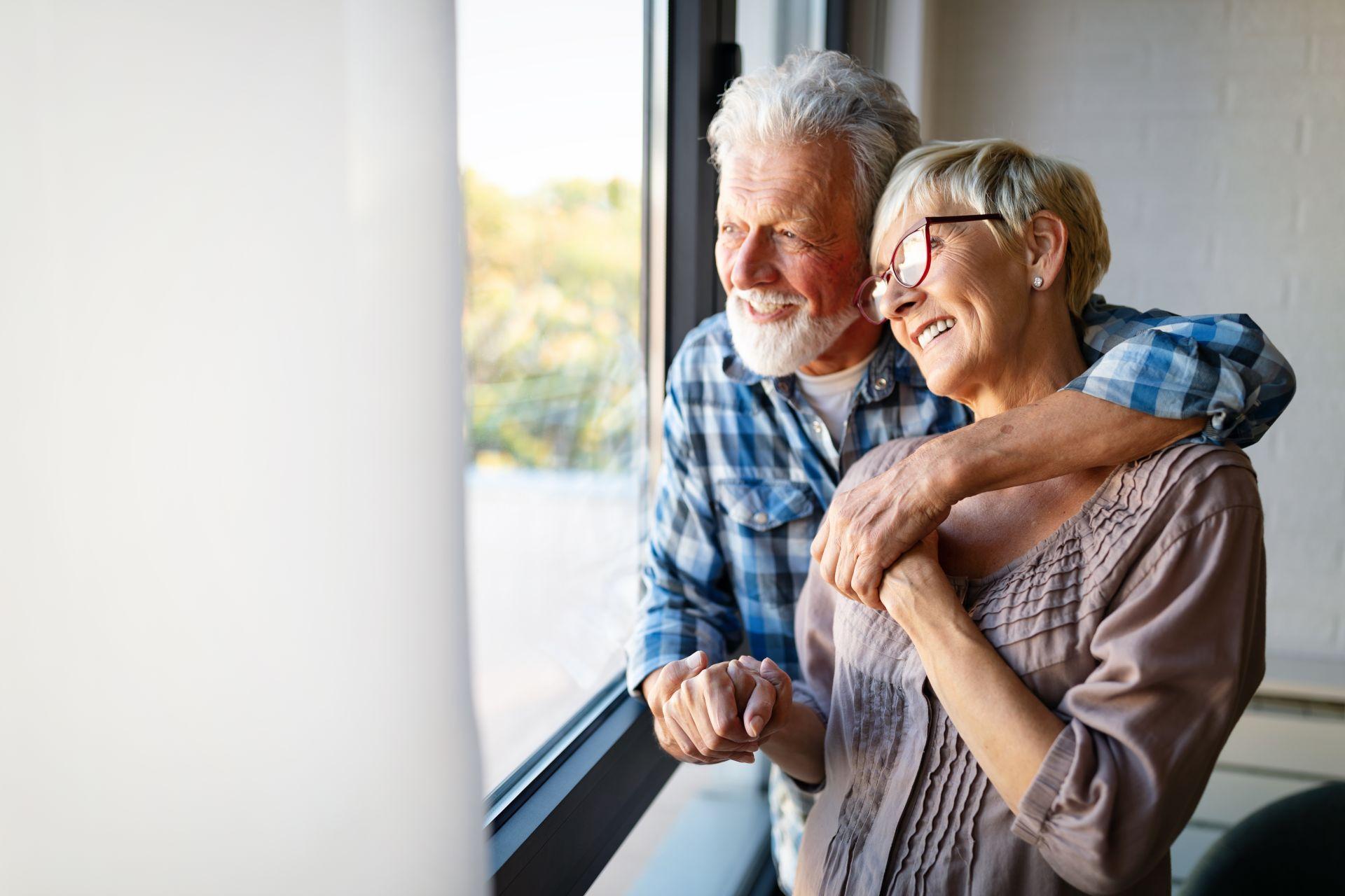 happy-smiling-senior-couple-embracing-together by window